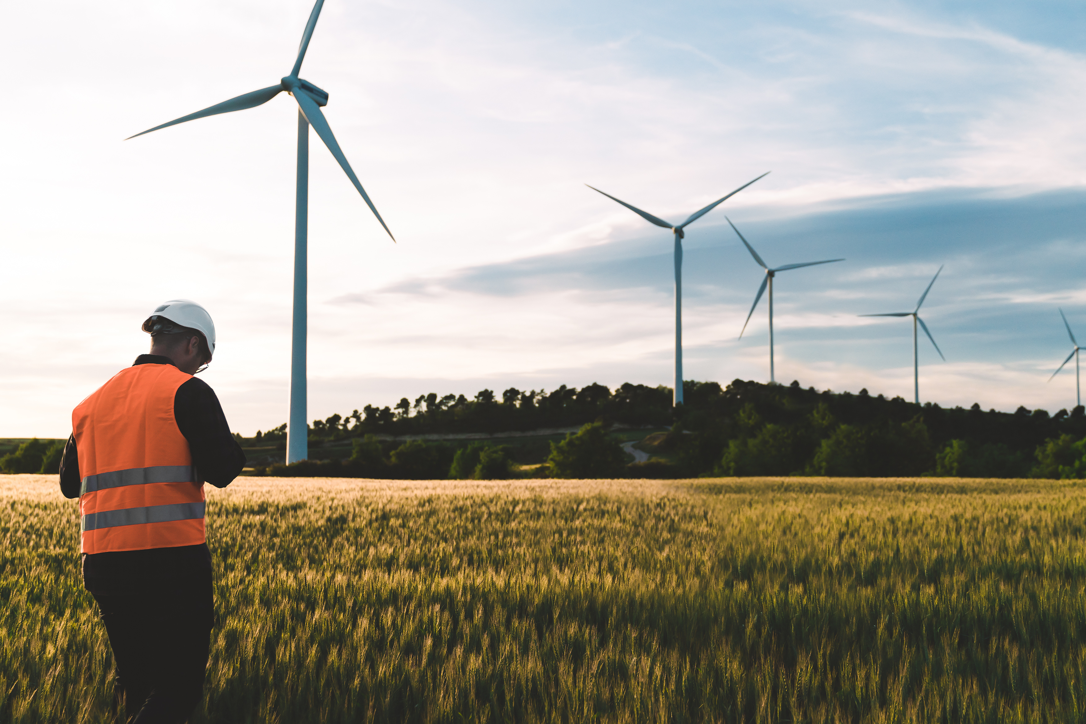 Construction worker walking towards windturbine in a field 